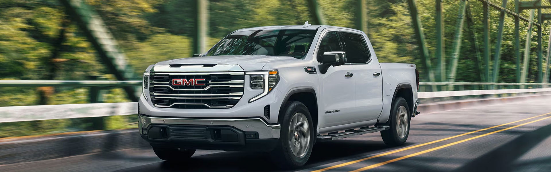White GMC Sierra pickup truck driving across a steel truss bridge